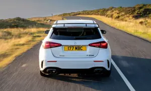 Biały Mercedes-AMG A45s pędzi po krętej drodze wśród wzgórz.