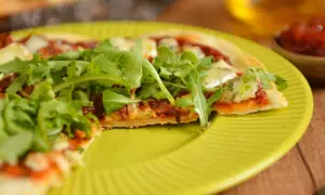 Pyszna pizza z patelni, z rukolą i serem, na żółtym talerzu.