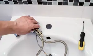 Hand montiert einen Wasserhahn, um das Waschbecken zu reparieren. Ein Schraubenzieher liegt bereit.