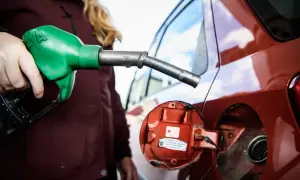En person fyller på moms på bensin vid en röd bil. En grön bensinpump är i handen.