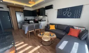 Nowoczesny salon z aneksem kuchennym, idealny na najem krótkoterminowy. Sofa, stolik kawowy, jadalnia i kuchnia.