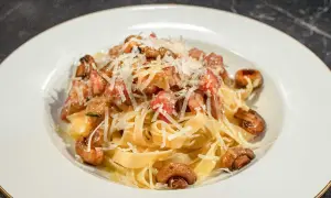 En tallrik med pasta alla boscaiola, toppad med riven parmesan och champinjoner.