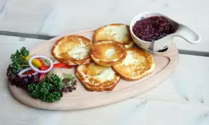 Smażony oscypek z żurawiną, podany z sałatką i pieczywem, na drewnianej desce.
