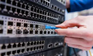 Dłoń podłącza niebieski kabel światłowodowy do portu na serwerze. To kluczowy element, jaki switch do światłowodu wybrać.