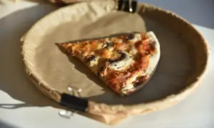 Kawałek pizzy z pieczarkami na brązowym papierze w okrągłym naczyniu.