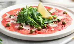 En tallrik med tunnskivad carpaccio di manzo, toppad med rucola, kapris, parmesan och en citronklyfta.