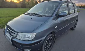 Szary Hyundai Matrix na tle zachodzącego słońca i zielonej łąki.