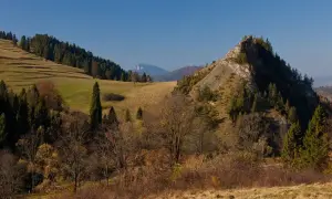 Jesienny krajobraz z dominującą, skalistą górą wysoką. Na zboczach drzewa iglaste i liściaste w jesiennych barwach.