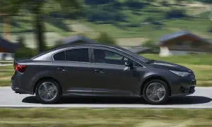 Ciemnoszara Toyota Avensis 2.0 D4D w ruchu, z rozmytym tłem górskiego krajobrazu.