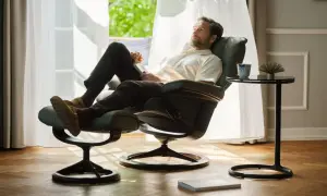 Man vilar i en bekväm Ekornes fåtölj med fotpall, njuter av ljuset från fönstret.