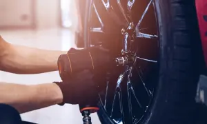 Mechanik w czarnych rękawiczkach używa klucza pneumatycznego do odkręcania śrub w feldze, przygotowując się do wymiany jednej opony.