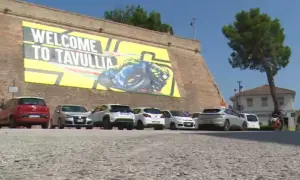 Benvenuti a Tavullia, la terra di Valentino Rossi! Un grande striscione giallo celebra il campione, con auto parcheggiate sotto.