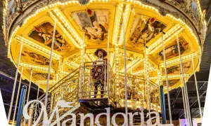 Złota karuzela w parku rozrywki Mandoria, ozdobiona malowidłami i światłami, z postacią w stroju z epoki.