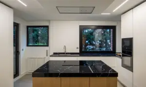 Cocina moderna con **fregadero en isla** de mármol negro y encimeras a juego. Muebles blancos y electrodomésticos integrados.