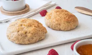 Två gyllene scones på en vit bricka, med hallon och sylt. Perfekt för fika med de godaste scones.