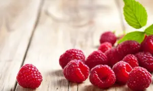 Maliny na drewnianym blacie, idealne na herbatę malinową w ciąży. Słodki smak lata dla przyszłej mamy.