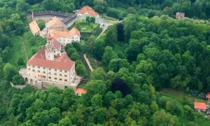 Zamek Nachod w Czechach, otoczony bujną zielenią, z charakterystyczną wieżą i czerwonymi dachami.