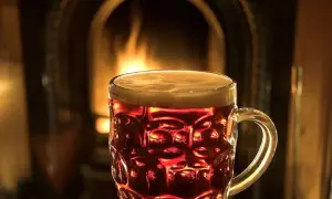 Bicchiere di birra ambrata con schiuma, davanti a un camino acceso. Un'atmosfera accogliente per gustare una birra calda.