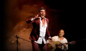 Un hombre con traje granate canta con pasión, su voz flamenco resuena mientras un guitarrista lo acompaña.