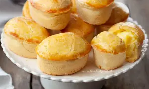 Un mucchio di pasticciotti pugliesi dorati e invitanti su un alzatina bianca.
