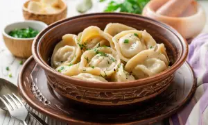Pielmieni co to? To pyszne, ręcznie robione pierożki, gotowane i posypane świeżymi ziołami, podane w glinianej misce.