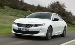 Biały Peugeot 508 jedzie po krętej drodze wśród zielonych wzgórz.
