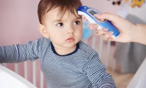 Mama mierzy temperaturę niemowlaka termometrem bezdotykowym. Dziecko ma na sobie pasiasty pajacyk.