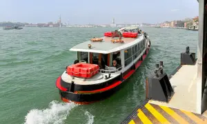 En man läser tidningen på en av båtarna i Venedig. I bakgrunden syns stadens silhuett.