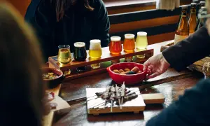 Degustazione di birre pregiate: un assortimento di diverse birre in bicchierini, accompagnate da stuzzichini e spiedini su un tavolo di legno.