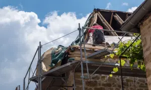 Un ouvrier travaille sur un toit en rénovation, une étape essentielle pour garantir ma prime logement décent. Le ciel bleu et les nuages blancs surplombent le chantier.