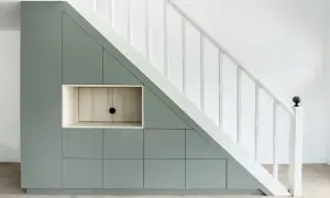 Aménagement sur mesure : un rangement sous escalier gris pâle avec des portes et une niche en bois clair.