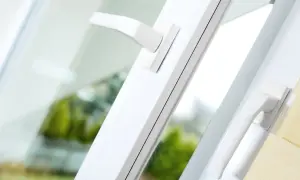 Białe, nowoczesne akcesoria okienne: dwa uchwyty okienne na tle zieleni.