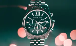Elegancki zegarek Michael Kors z ciemną tarczą i srebrną bransoletą, na tle rozmytych świateł.