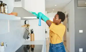 Donna con guanti pulisce la cappa della cucina con uno spray.
