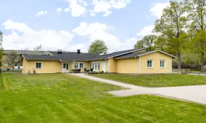 Gult behandlingshem för vuxna med gräsmatta och träd.