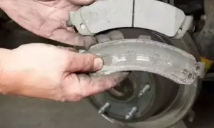 Mani sporche confrontano pastiglie freni nuove e usurate, mostrando il **spessore minimo pastiglie freni** raggiunto da quelle vecchie.