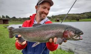 Glücklicher Angler hält stolz einen großen Regenbogenforelle, ein toller Fang beim LImfjord angeln.