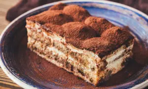 Une part de tiramisu, saupoudrée de cacao, sur une assiette bleue. Un délice qui évoque tous les ingrédients du tiramisu.