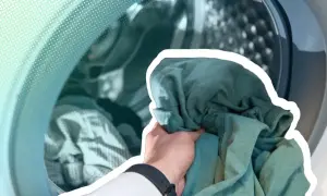 Hand lädt grüne Kleidung in eine Waschmaschine. Zeit, die neue Kleidung zu waschen und sie frisch zu machen.