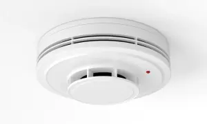 Détecteur de fumée blanc, rond, fixé au plafond. Un petit voyant rouge est allumé. Un détecteur fumée obligatoire pour votre sécurité.