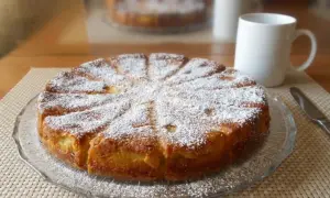 Gâteau fondant aux pommes et mascarpone, saupoudré de sucre glace, prêt à être dégusté avec une tasse de café.