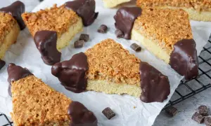 Dreiecke von einem Nussecken Rezept, mit Schokoladenboden und knuspriger Nussdecke, auf Backpapier arrangiert.