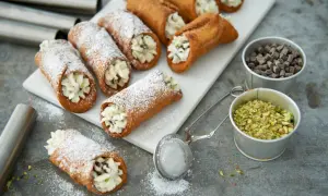 Färska cannoli med krämig fyllning, pudrade med florsocker. Ingredienser för ett perfekt cannoli recept syns bredvid.