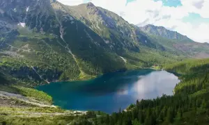 Malownicze Morskie Oko, idealne na górską trasę. Woda odbija niebo, otoczona zielonymi lasami i skalistymi szczytami.