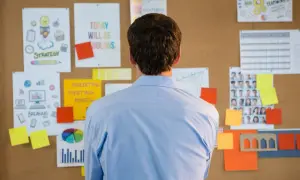 Uomo osserva bacheca con grafici, foto e note. I turni di lavoro devono essere esposti chiaramente per tutti.