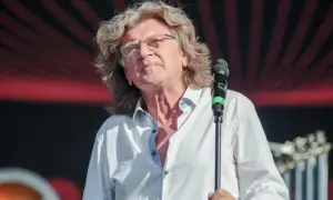 Zbliżenie na mężczyznę w białej koszuli z rozpiętym kołnierzykiem, śpiewającego do mikrofonu.