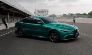 Zielona Alfa Romeo Giulia Quadrifoglio na torze wyścigowym, z wieżą kontrolną w tle.