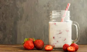Kefir z truskawkami w słoiku z uchem, obok świeże truskawki na drewnianym stole.