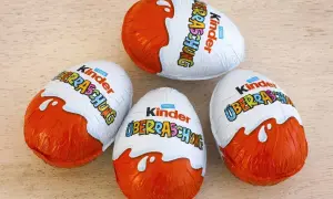 Cztery jajka Kinder Niespodzianka na drewnianym tle.