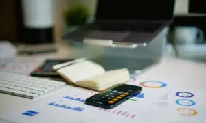 Scrivania con laptop, tastiera, quaderno aperto, calcolatrice su grafici. Pianificazione della tassazione premio produzione 2026.